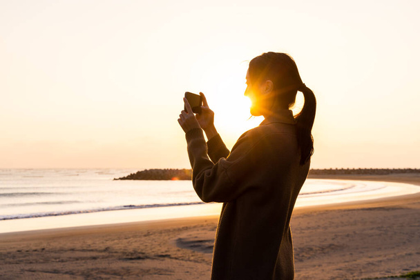 Силует жінки використовують камеру, щоб сфотографуватися на заході сонця на пляжі
 - Фото, зображення