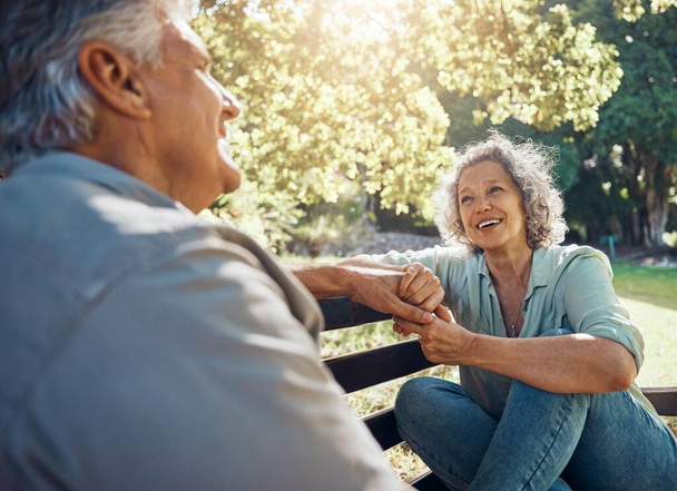 Ancianos, pareja y feliz en el banco en el jardín para la conversación, la vinculación y la felicidad por los árboles en verano. Hombre, mujer y jubilación muestran amor, relajarse y sonreír juntos en la naturaleza con el sol en el parque. - Foto, Imagen