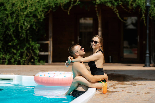 chico y una chica en trajes de baño son relajantes, tomar el sol y divertirse cerca de la piscina azul - Foto, Imagen