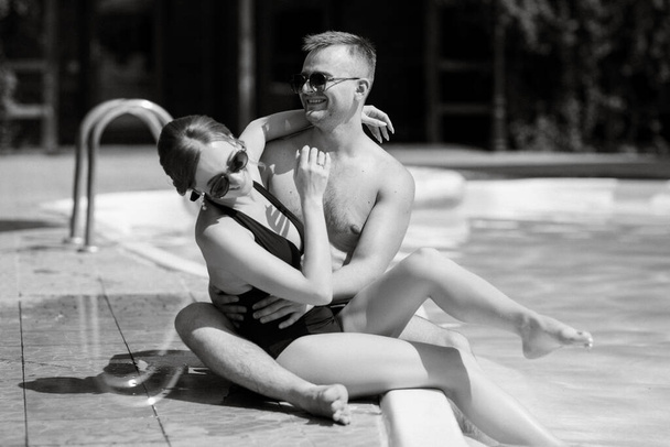 guy and a girl in bathing suits are relaxing, sunbathing and having fun near the blue pool - Photo, Image