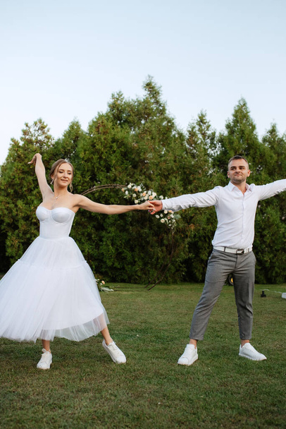 the first dance of the groom and bride in a short wedding dress on a green meadow - Photo, Image