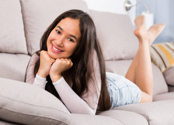Young glad woman lying on cozy sofa and smiling at home - Foto, Bild