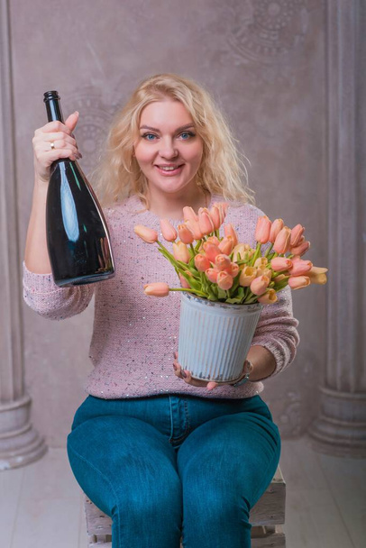 Ωραία χαρούμενη γυναίκα γιορτάζει με ένα μπουκάλι σαμπάνια και λουλούδια. Χαρούμενη διάθεση - Φωτογραφία, εικόνα