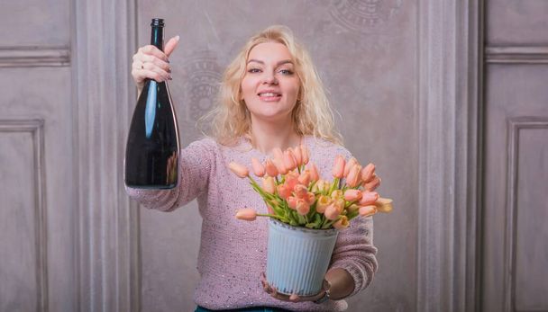 Милая счастливая женщина празднует с бутылкой шампанского и цветами. Счастливого настроения - Фото, изображение