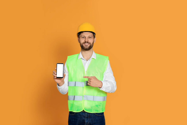 Man in reflective uniform showing smartphone on orange background - 写真・画像