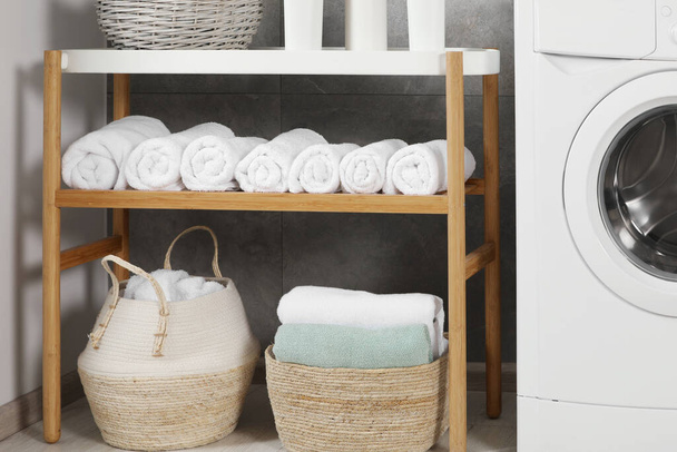 Wooden shelf and wicker baskets with soft terry towels in bathroom - Foto, Bild