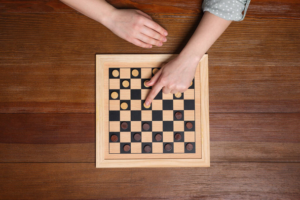 Playing checkers. Woman thinking about next move at wooden table, top view - Photo, image