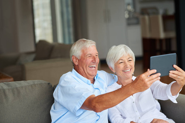 Vamos a mostrarles cómo una pareja debe hacer una selfie. una pareja de ancianos tomando una selfie con su tableta en casa - Foto, imagen