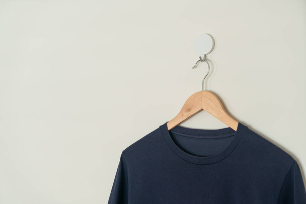 navy t-shirt hanging with wood hanger on wall - Φωτογραφία, εικόνα
