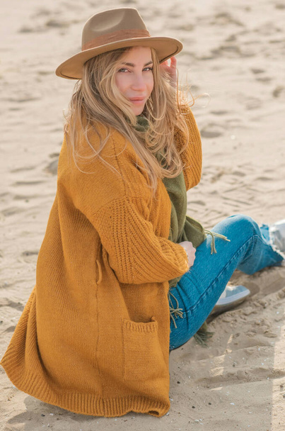 Woman in wool yellow cardigan, fedora hat and blue jeans at the beach, new collection, fashionable trend - Fotografie, Obrázek