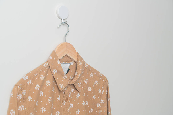 hanging beige shirt with wood hanger on wall - Фото, зображення
