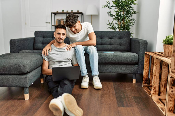 Dos hombres hispanos en pareja usando laptop abrazándose en casa - Foto, Imagen