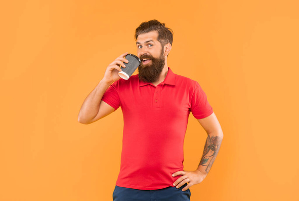 Happy man drinking coffee from disposable cup with arm akimbo yellow background, takeaway. - Foto, Bild