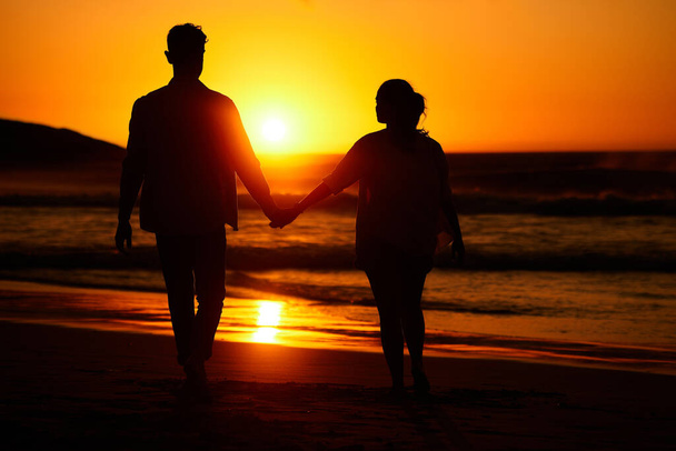 Ocean sunset, couple walking and beach water at night or woman and man love holding hands at sea summer vacation. Travel together, honeymoon silhouette and bonding on holiday sky sunlight in nature. - Photo, Image