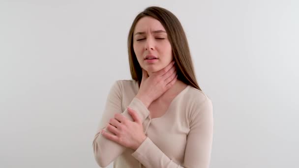 Mujer joven malsana difícil de tragar tener malestar pérdida de la voz dolor de garganta chica sosteniendo su mano a su garganta encogida sobre un fondo blanco en el estudio emociones desagradables de la enfermedad - Metraje, vídeo