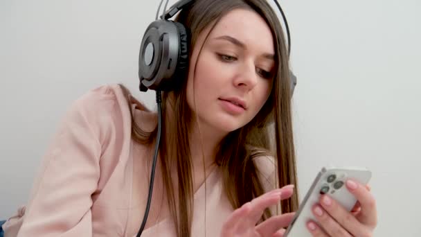 chica joven con un teléfono en sus manos está escribiendo un mensaje de escuchar música de trabajo en casa consejos de aprendizaje en línea para pasar una mirada examen en Internet respuestas a la prueba de entradas de clase - Metraje, vídeo