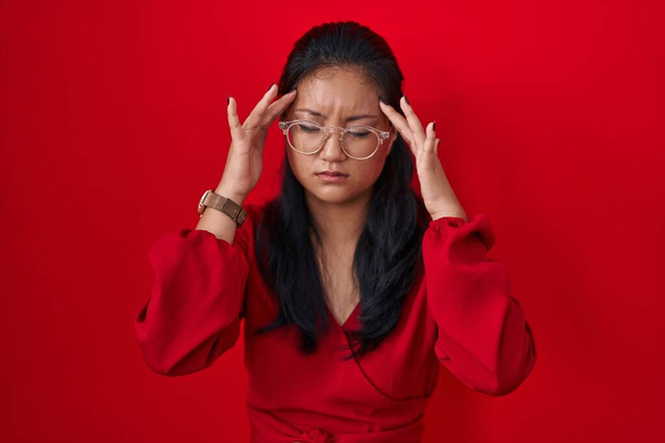 Mujer joven asiática de pie sobre fondo rojo con la mano en la cabeza, dolor de cabeza porque el estrés. padecer migraña.  - Foto, imagen