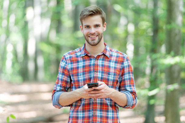 mężczyzna wysyłający wiadomości przez telefon nosi koszulę w kratkę. Zdjęcie człowieka wysyłającego wiadomości przez telefon w lesie. mężczyzna wysyła wiadomości przez telefon na zewnątrz. mężczyzna wiadomości przez telefon na zewnątrz. - Zdjęcie, obraz