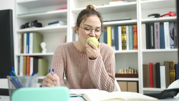 Junge schöne hispanische Studentin schreibt an Notizbuch und isst Apfel in der Bibliothek Universität - Foto, Bild