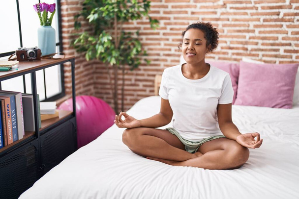 African american woman doing yoga exercise sitting on bed at bedroom - Photo, Image