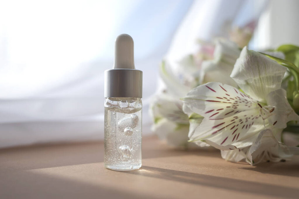 Tropfflasche aus Glas mit feuchtigkeitsspendender Lotion auf dem Hintergrund eines Blumenstraußes. Gesichtspflegekonzept. - Foto, Bild
