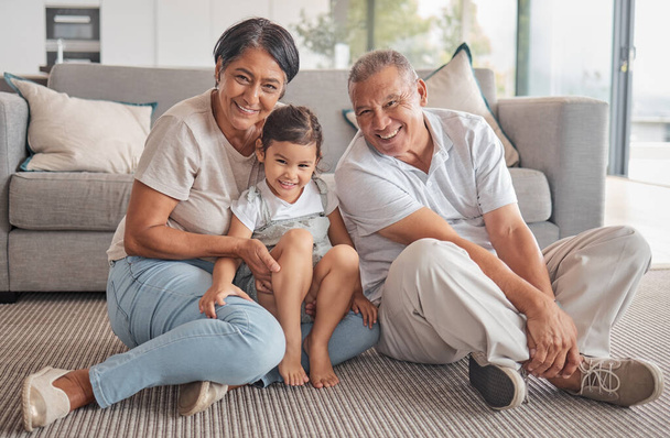Girl, hug and grandparents with love, care and relax in family home together. Portrait of happy child, smile senior grandma and laugh elderly grandpa bond and play together in the living room floor. - Фото, зображення
