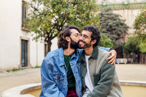 young man kissing tenderly his boyfriends cheek, concept of urban lifestyle and love between people of the same sex, copy space for text - Фото, зображення
