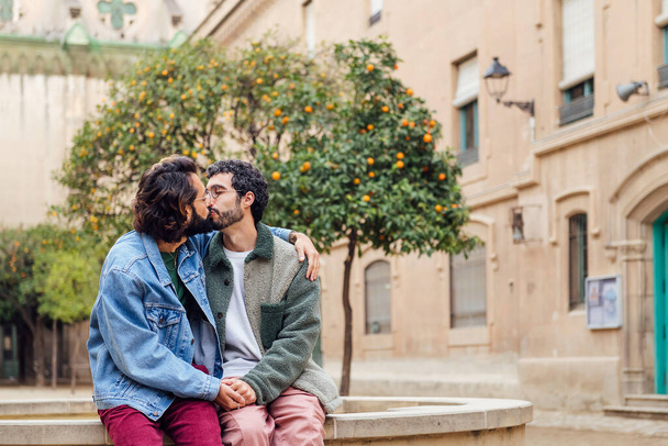 happy young couple of gay men kissing tenderly holding hands, concept of urban lifestyle and love between people of the same sex, copy space for text - Φωτογραφία, εικόνα