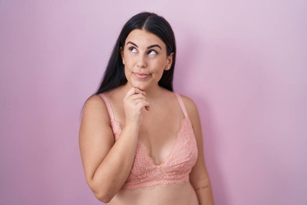 Young hispanic woman wearing pink bra with hand on chin thinking about question, pensive expression. smiling and thoughtful face. doubt concept.  - Fotoğraf, Görsel