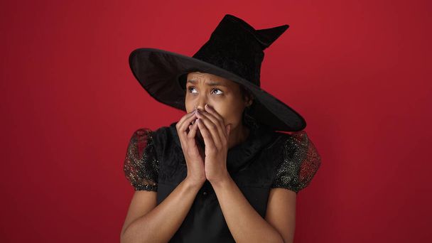 Afroamerykanka ubrana w strój czarownicy robi gest strachu nad odizolowanym czerwonym tłem - Zdjęcie, obraz