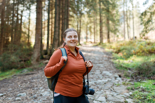 Alleinreisende Frau wandert auf Fußweg im Herbstwald. Glückliche rothaarige Person in aktiver Trekking-Kleidung beim Wandern auf Naturrücken. - Foto, Bild