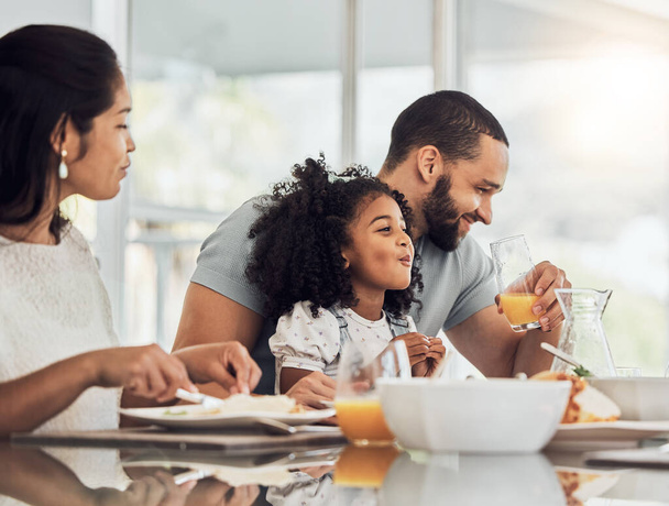 Happy family, breakfast and eating at table in home, talking or discussion together. Love, support and comic man, woman and girl child laughing, care and bonding drinking orange juice and having food. - Photo, Image