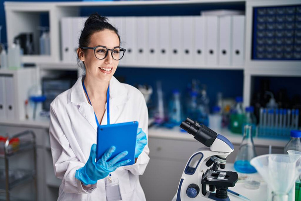 Молода біла жінка-науковець посміхається впевнено використовуючи тачпад в лабораторії
 - Фото, зображення