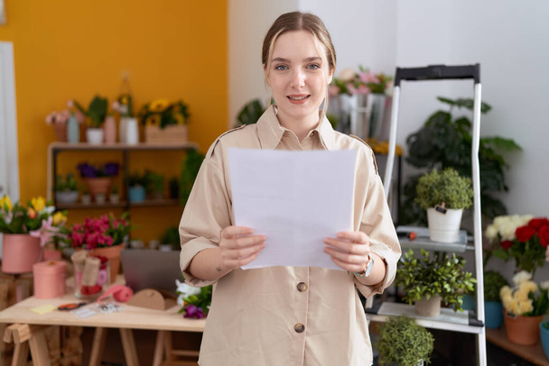 Young caucasian woman florist smiling confident reading document at flower shop - Fotoğraf, Görsel