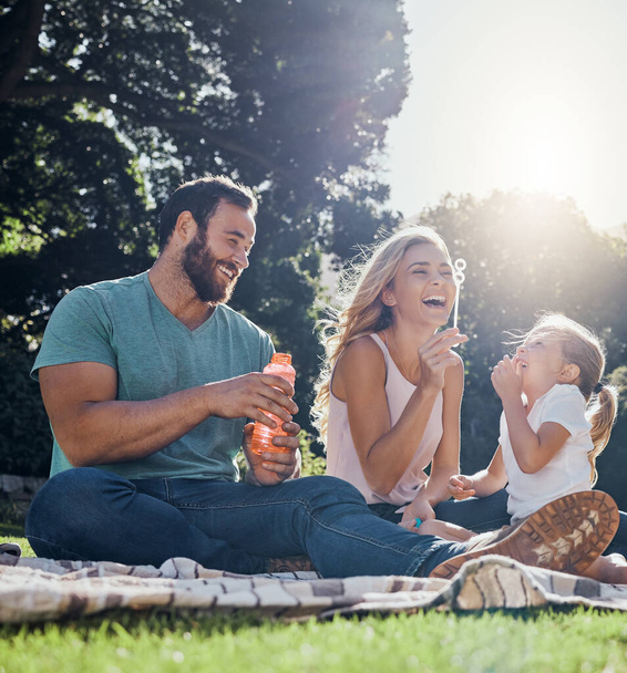 Familia, feliz y burbujas con picnic en el parque juntos para el verano, relajarse y la naturaleza. Sonrisa, primavera y paz con los padres jugando con la niña en el campo para la juventud, el estilo de vida y la felicidad. - Foto, imagen