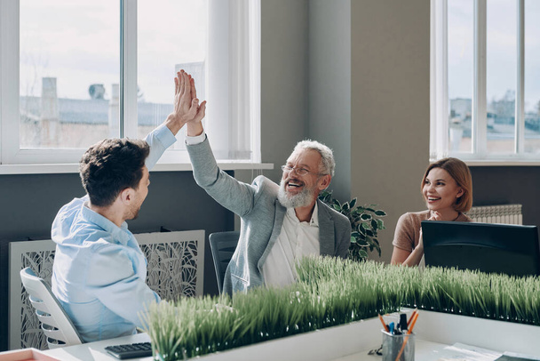 Cheerful business people celebrating success in the office while two men giving high five - Fotoğraf, Görsel