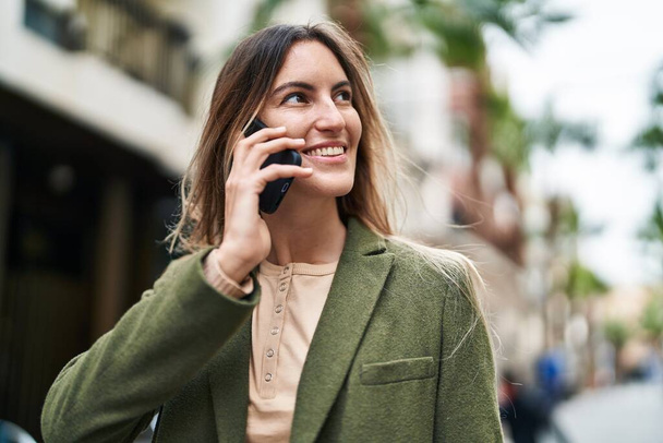 Mujer joven sonriendo confiada hablando en el teléfono inteligente en la calle - Foto, imagen