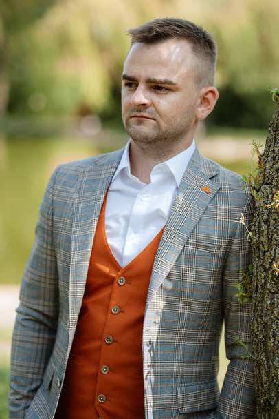 portrait of the groom in a gray suit and an orange vest and white sneakers - Foto, Imagen