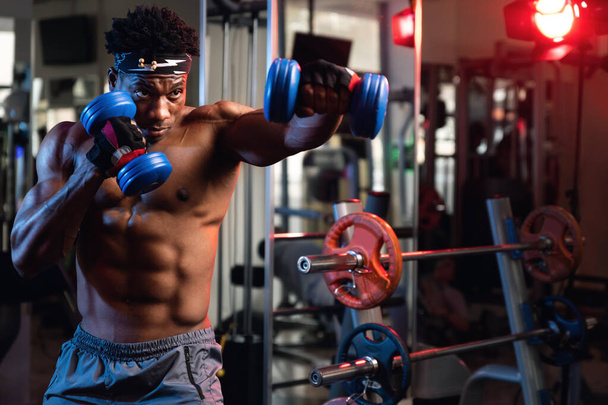 Portrait of a 20s black muscular male fist working out with dumbbells - 写真・画像