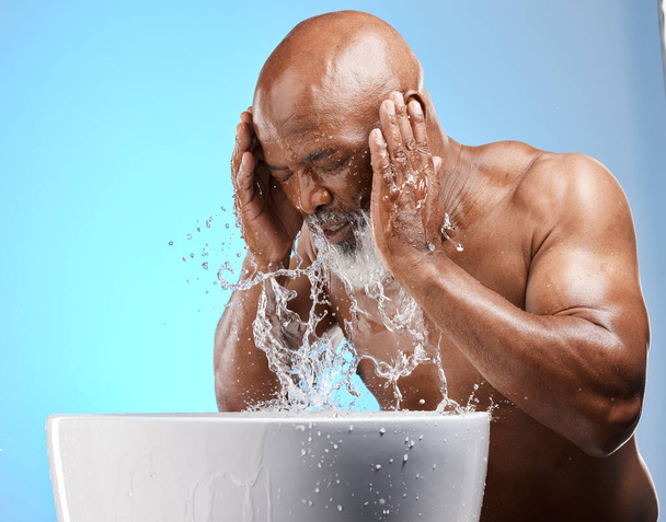 Skincare, water splash and black man for senior skincare while washing face for a glow, healthy and clean skin on blue background. African model in studio with basin for dermatology and self care. - Foto, afbeelding