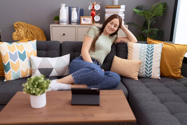 Fiatal gyönyörű nő néz videó érintőpad ül kanapén otthon - Fotó, kép