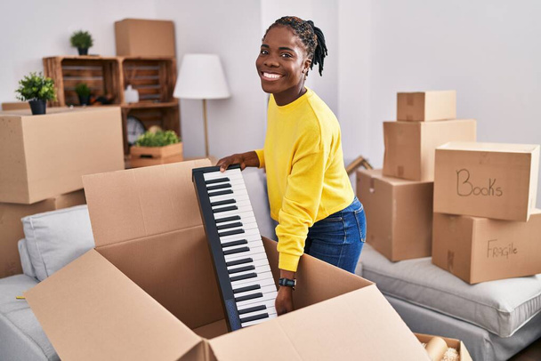 Africano americano mulher sorrindo confiante unboxing teclado em nova casa - Foto, Imagem