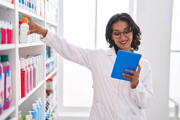 fiatal gyönyörű spanyol nő gyógyszerész használ touchpad gazdaság gyógyszer a gyógyszertárban - Fotó, kép