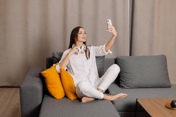 Onnellinen ja hymyilevä valkoihoinen nainen kuulokkeet käyttää matkapuhelinta on webcam digitaalinen online-viestintä kotona. - Valokuva, kuva