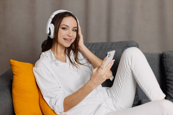 Teen  student girl wear headphones  using smartphone and watching online video course at home - Foto, Imagem