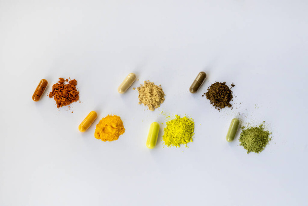 Opened and whole capsules of dietary supplements on a white background. Various tablets and vitamins. From top right to left: curcumin, Coenzyme q10, vitamin C, quercetin, ant tree bark, vitgrass. - Zdjęcie, obraz