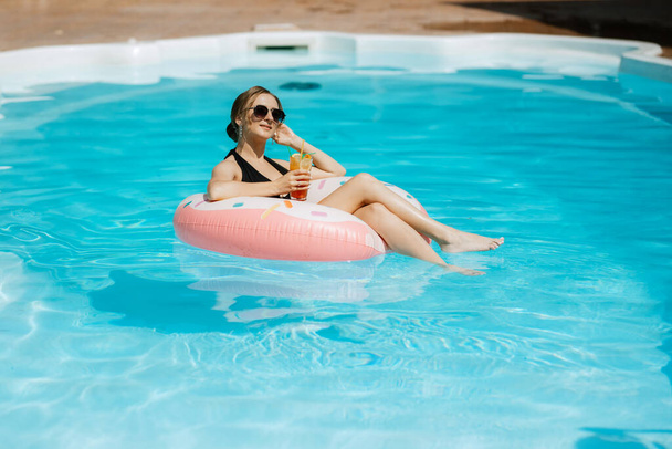 дівчина в чорному купальнику плаває на надувному колі в блакитному басейні
 - Фото, зображення