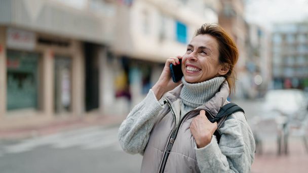 Keski-ikä latino nainen hymyilee luottavainen puhuu älypuhelimeen kadulla - Valokuva, kuva