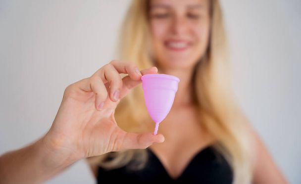 Young beautiful woman at home holding a menstrual cup in her hands. - Zdjęcie, obraz