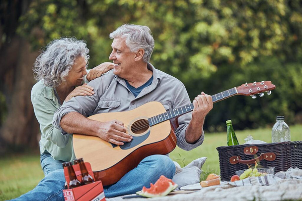 Musiikki, kitara ja vanhempi pari huviretkellä puistossa nauravat ruoalla, juomilla ja romantiikalla eläkkeellä. Luonto, rakkaus ja vanhusten mies ja onnellinen nainen romanttinen päivämäärä ruoho kesällä viikonloppuna - Valokuva, kuva